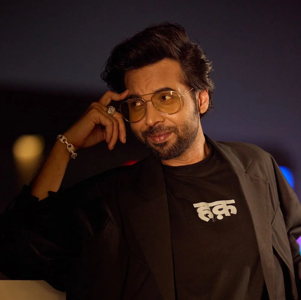 Abhishek Bannerjee wearing glasses and a black jacket posing against a dark background