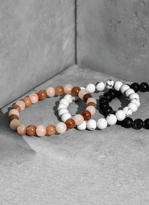 Three orionz beaded bracelets in brown, white, and black on a gray surface.