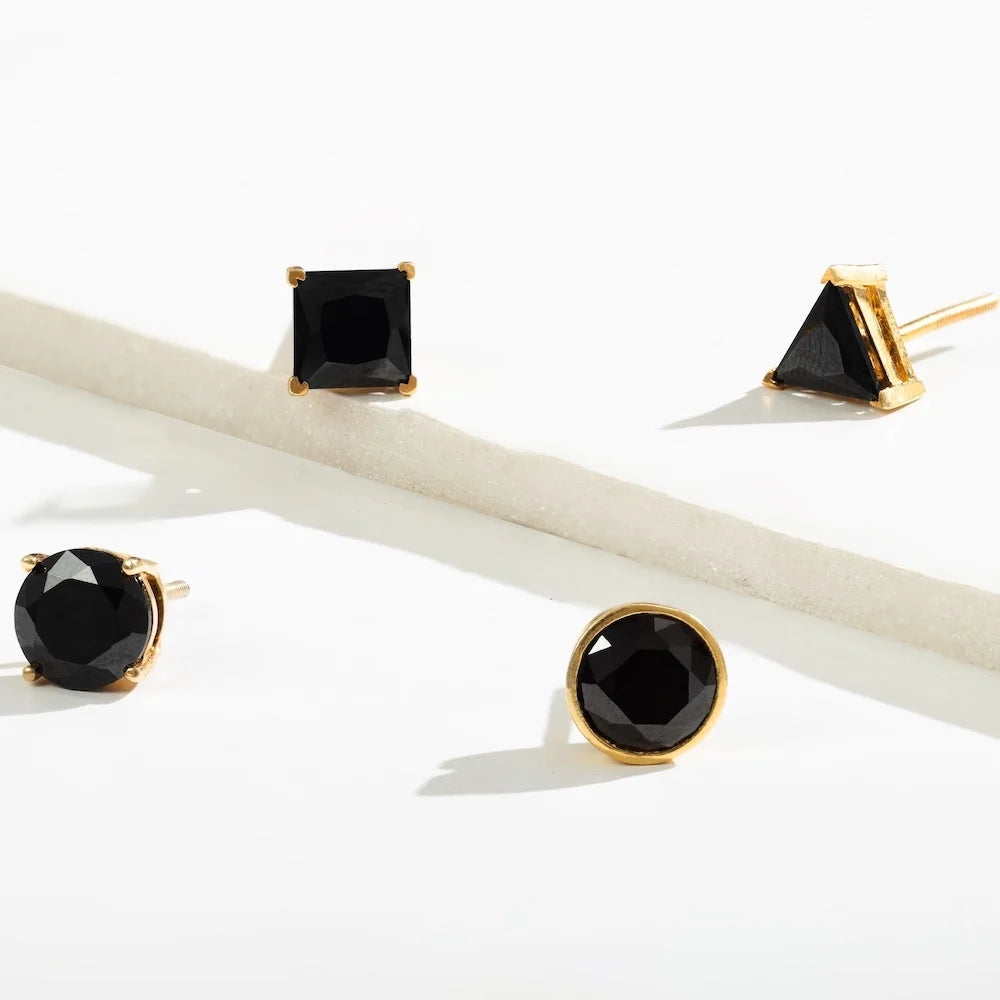 Four pairs of black gemstone orionz earrings with gold settings on a white background