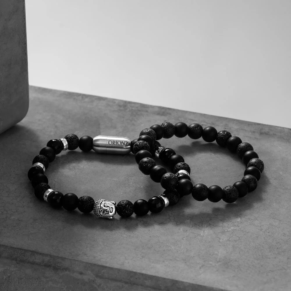 Two black orionz beaded bracelets with silver tags on a gray surface