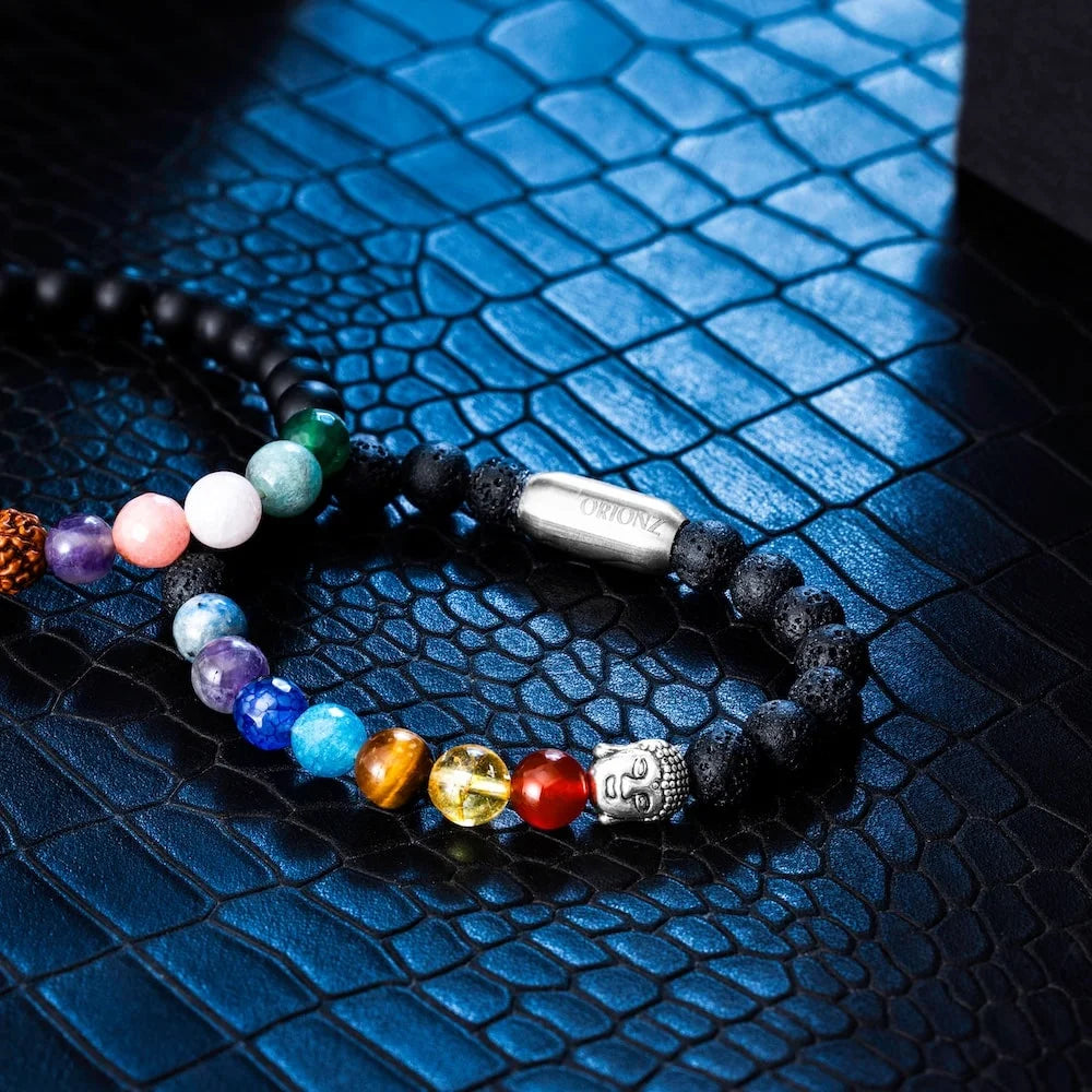 Multicolored orionz beaded bracelet with a silver Buddha charm on a textured blue surface