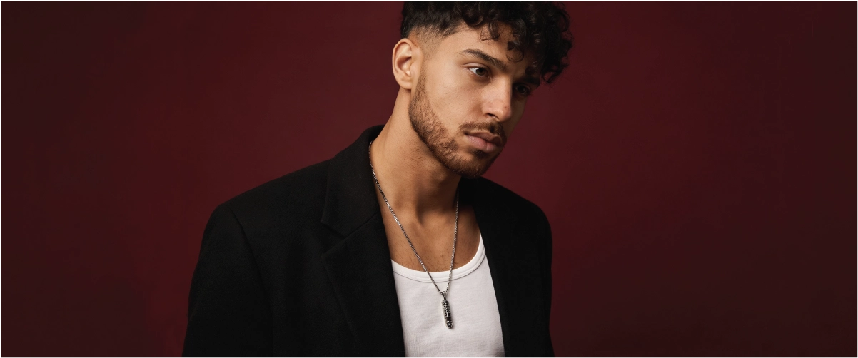 Man wearing a black blazer over a white shirt against a dark red background