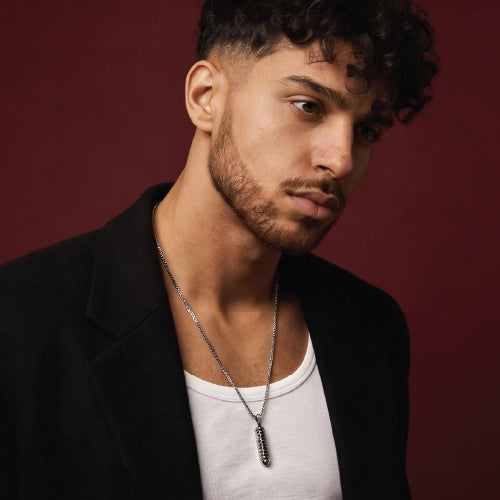 Man wearing a black jacket and white shirt with a necklace against a red background