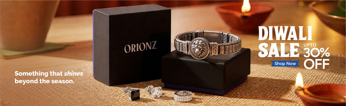 A silver-toned Orionz watch with a lion emblem on the dial, displayed on a black stand next to its black Orionz box. The scene is set on a burlap surface with warm lighting from lit clay lamps, alongside promotional text for a Diwali sale.