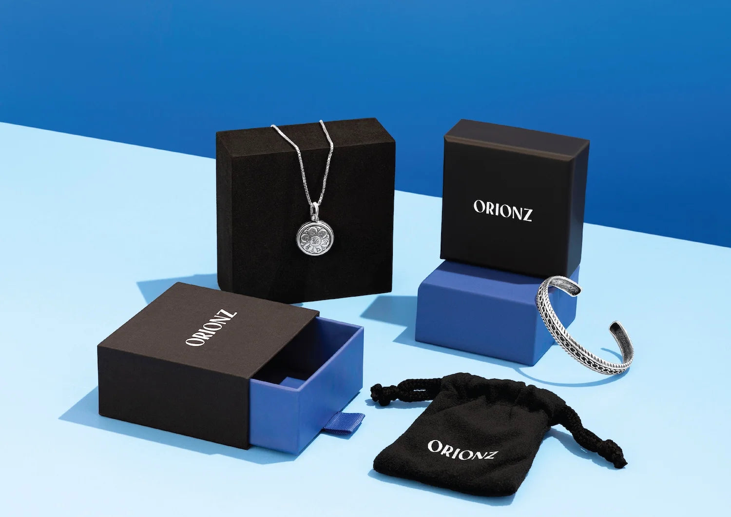 Jewelry set with necklace, bracelet, and pouch on Orionz branded boxes against a blue background