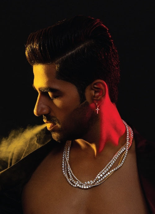 Man wearing an orionz necklace with a cross earring against a dark background