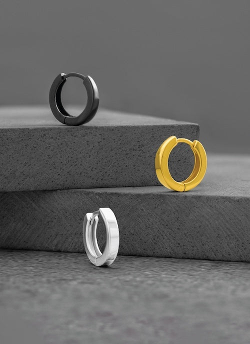 Three orionz hoop earrings in black, gold, and silver on a gray surface.