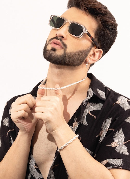 Man wearing sunglasses and a patterned shirt with orionz jewelry on a white background