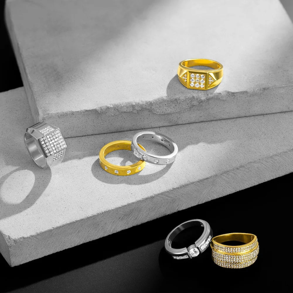 Collection of gold and silver rings with diamond accents on a stone surface.