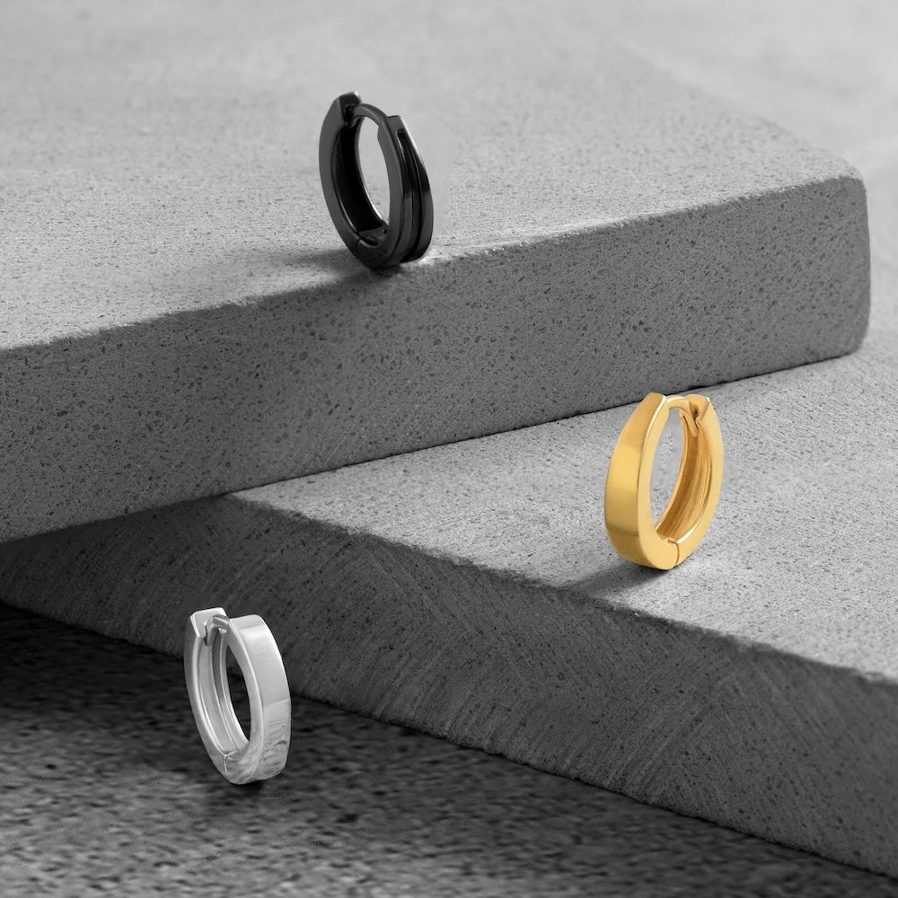 Three orionz hoop earrings in black, gold, and silver on a textured stone surface.