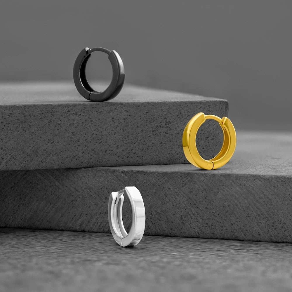 Three orionz hoop earrings in black, gold, and silver on a gray surface.