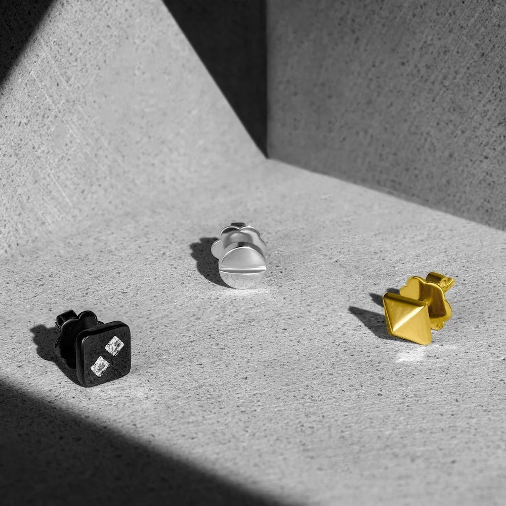 Three pairs of orionz earrings in black, silver, and gold on a textured surface.